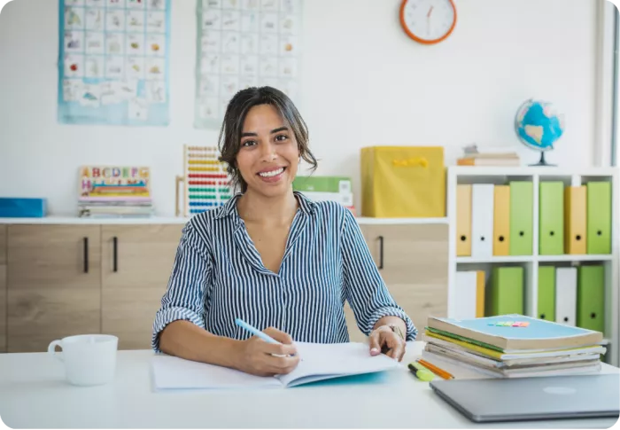 Maitresse d'école assise à un bureau, dans une salle de classe, étant en train d'écrire